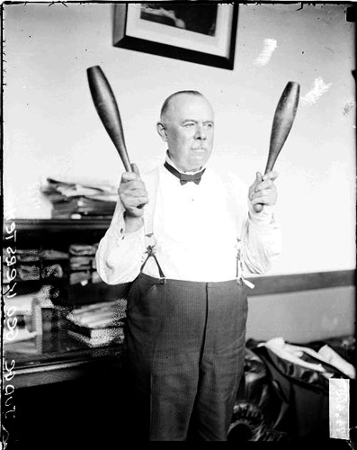 Judge George Kersten standing in a room and exercising with two juggling pins (1922)
